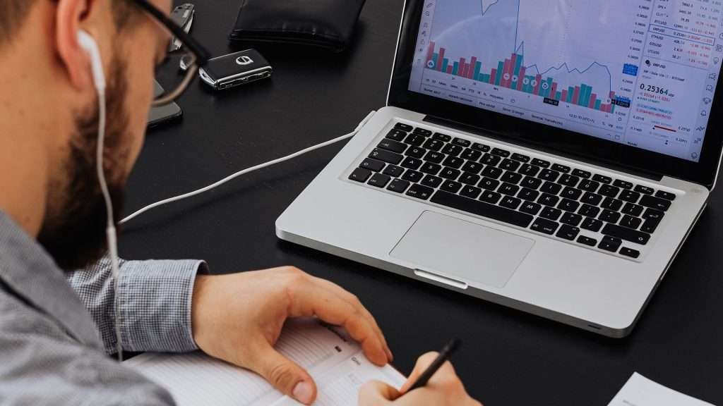 Man taking notes while looking at screen with crypto currency diagrams